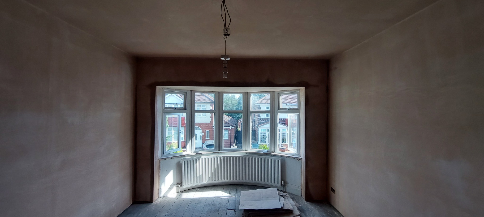 Pokój po nałożeniu gładzi szpachlowej na ścianach, widoczne okno wykuszowe i grzejnik, przygotowany do dalszych prac wykończeniowych.