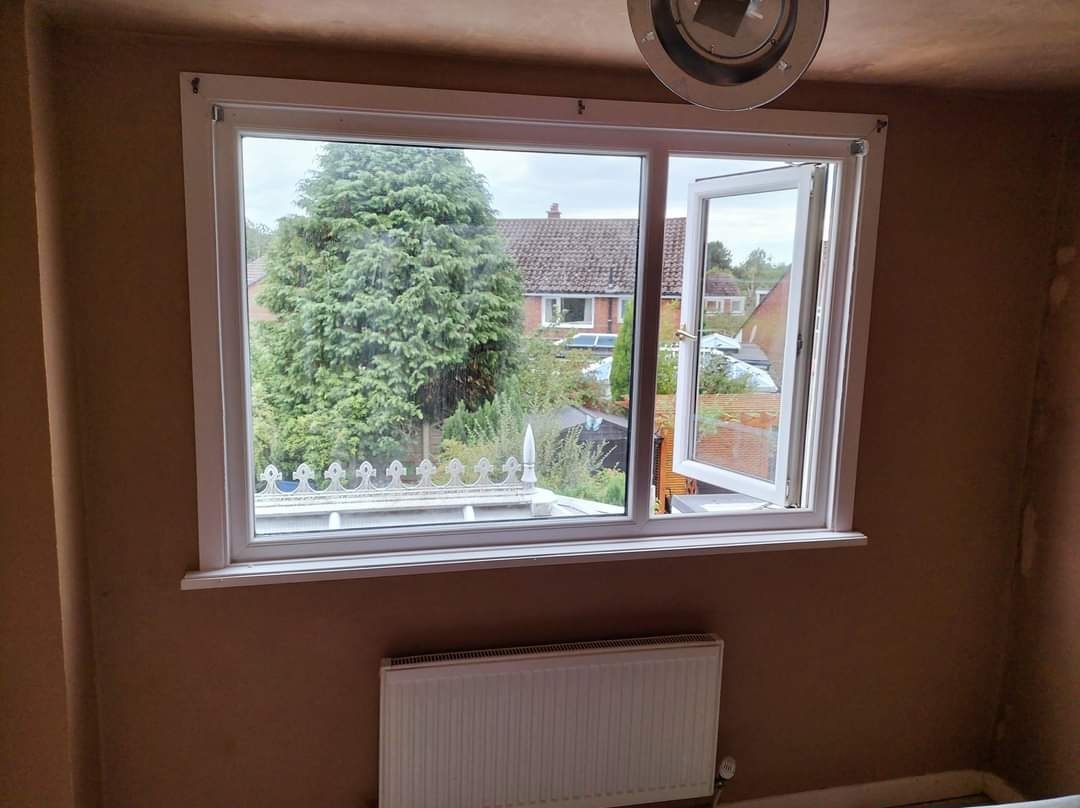 Pokój w trakcie przygotowania do malowania: ściany po szpachlowaniu, okno z widokiem na zieleń, grzejnik pod oknem.