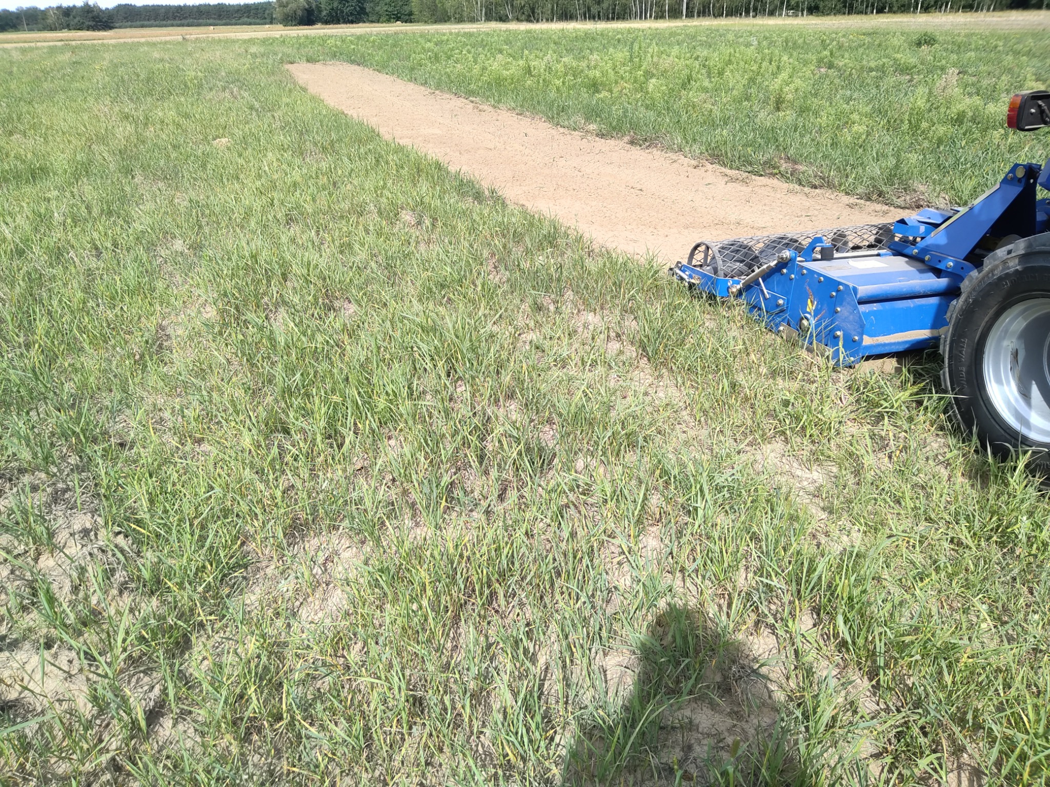 Ciągnik z broną talerzową wyrównuje pas ziemi na polu, przygotowując teren pod uprawę, widoczne świeżo obrobione podłoże i cień operatora.
