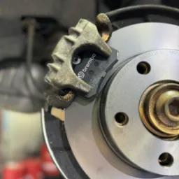 Nowe klocki hamulcowe marki Brembo zamontowane na tarczy hamulcowej. Widoczne oznaczenia na klockach i tarczy.