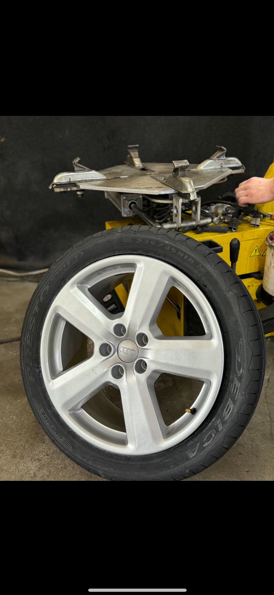 Srebrna felga Audi z oponą Debica na tle montażownicy do opon w warsztacie w Warszawie. Widoczny fragment dłoni pracownika.