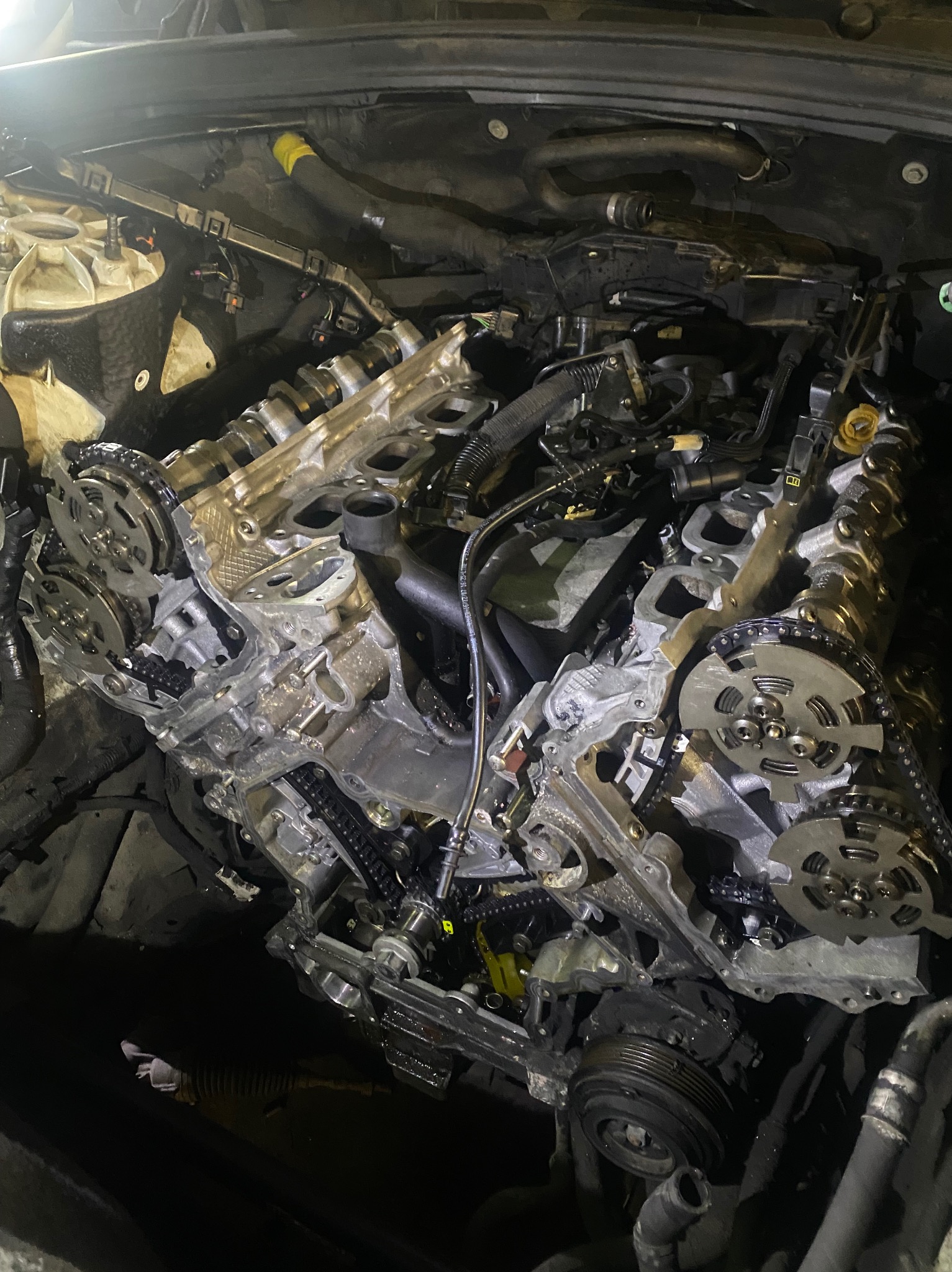 Widok z góry na rozłożony silnik samochodowy z widocznymi łańcuchami rozrządu, kołami zębatymi i elementami głowicy cylindrów w trakcie naprawy lub diagnostyki.