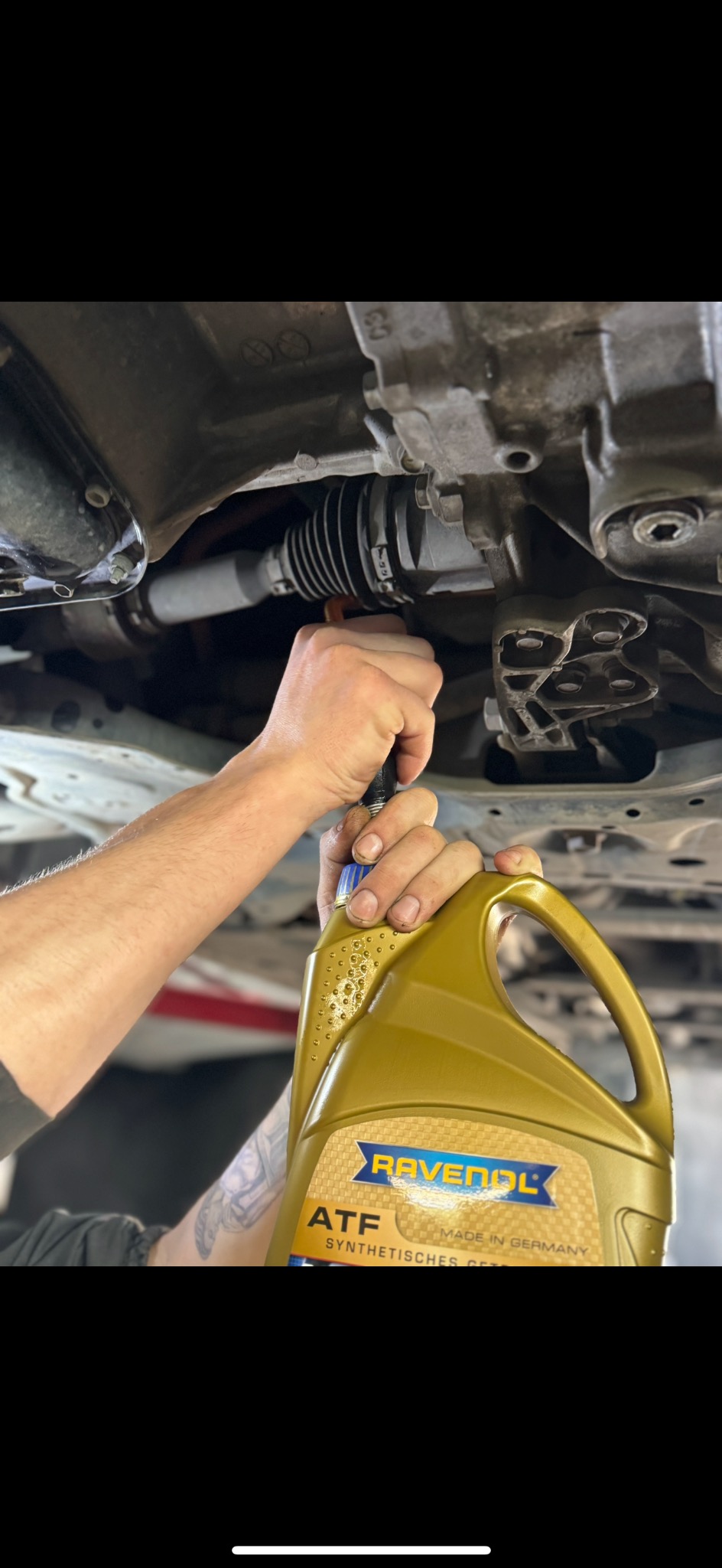 Wymiana płynu ATF marki Ravenol w przekładni samochodu, widoczne ręce mechanika i element podwozia.