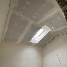 KAER Krzysztof Ratajczak - Pokój ze skośnym sufitem po montażu płyt gipsowo-kartonowych i szpachlowaniu, widoczne okno dachowe i wystające przewody. Ściany przygotowane do malowania.