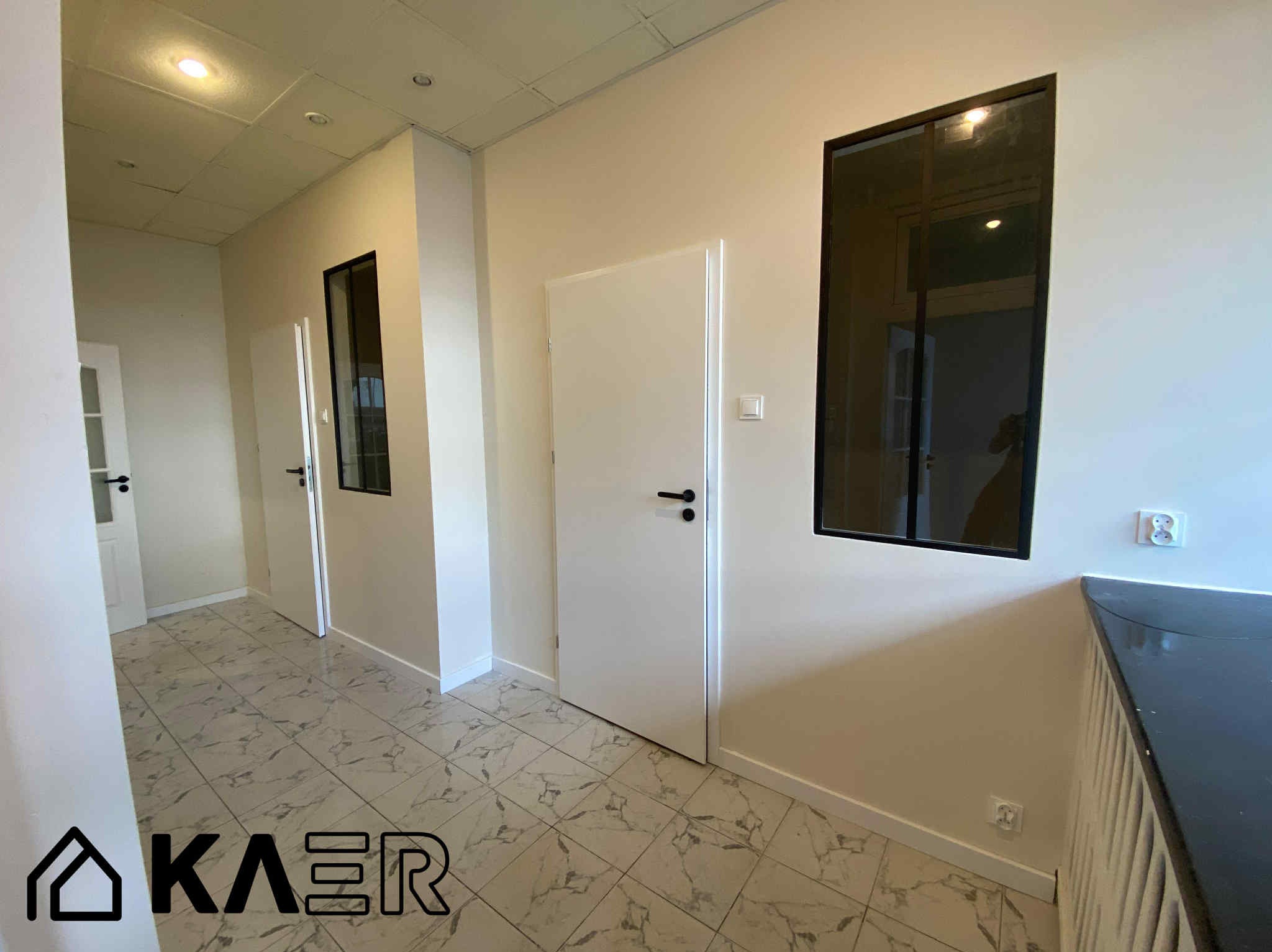 Korytarz po remoncie z białymi ścianami, drzwiami i marmurową podłogą. Okna z czarnymi ramami. Widoczny fragment blatu i gniazdka elektryczne.