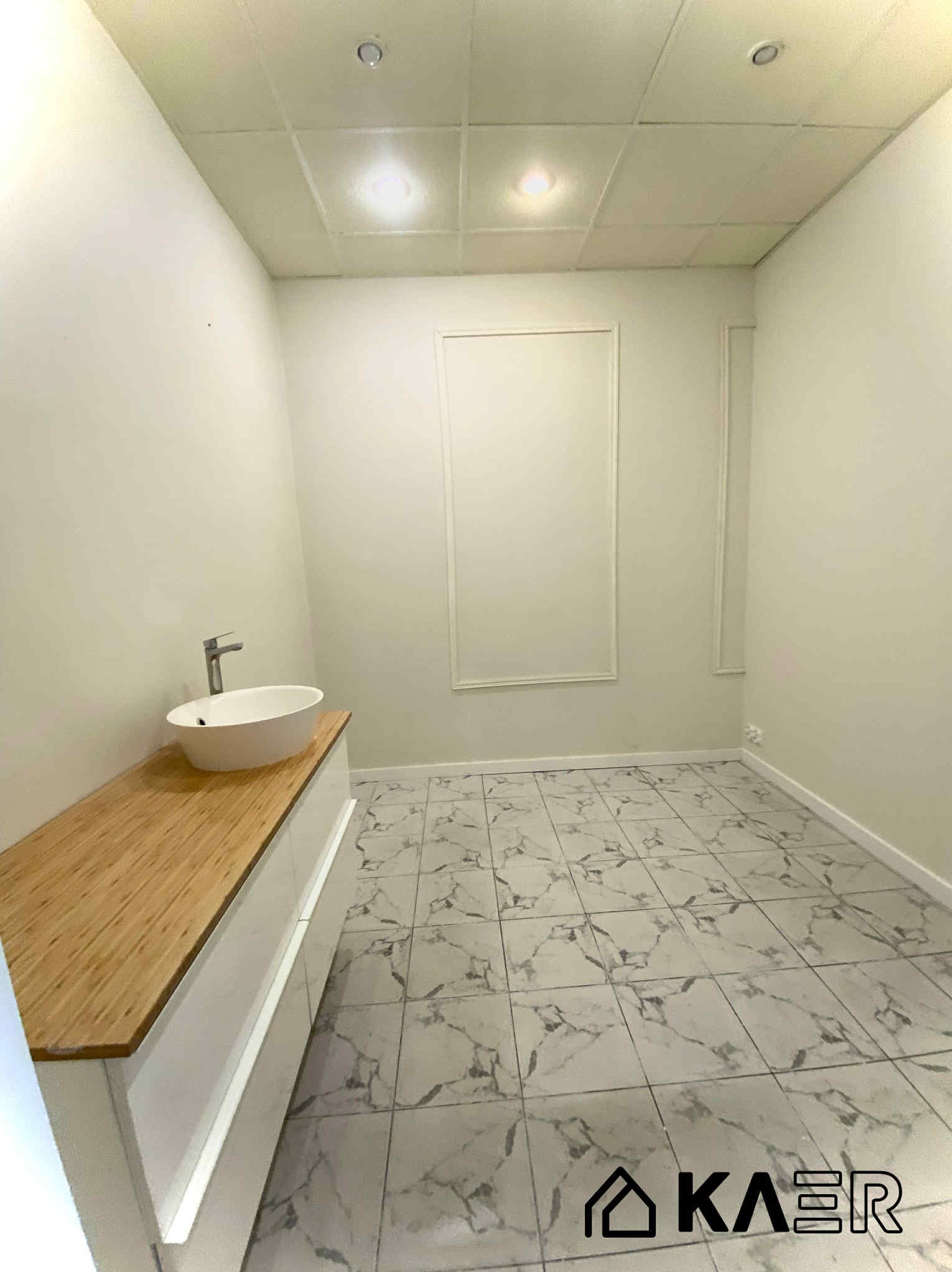 Jasne wnętrze łazienki po remoncie: białe ściany z dekoracyjną listwą, marmurowe płytki podłogowe, umywalka na drewnianym blacie. Minimalistyczny design.