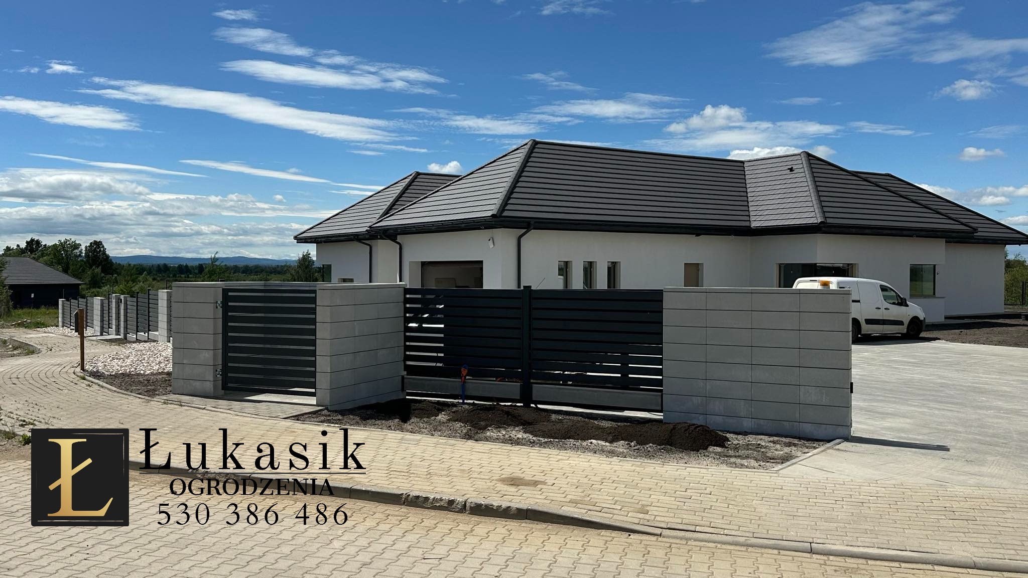 Nowoczesne ogrodzenie panelowe z betonowymi słupkami, brama wjazdowa z czarnymi, poziomymi przęsłami na tle białego domu z szarą dachówką i błękitnego nieba, widoczny logotyp firmy na pierwszym...