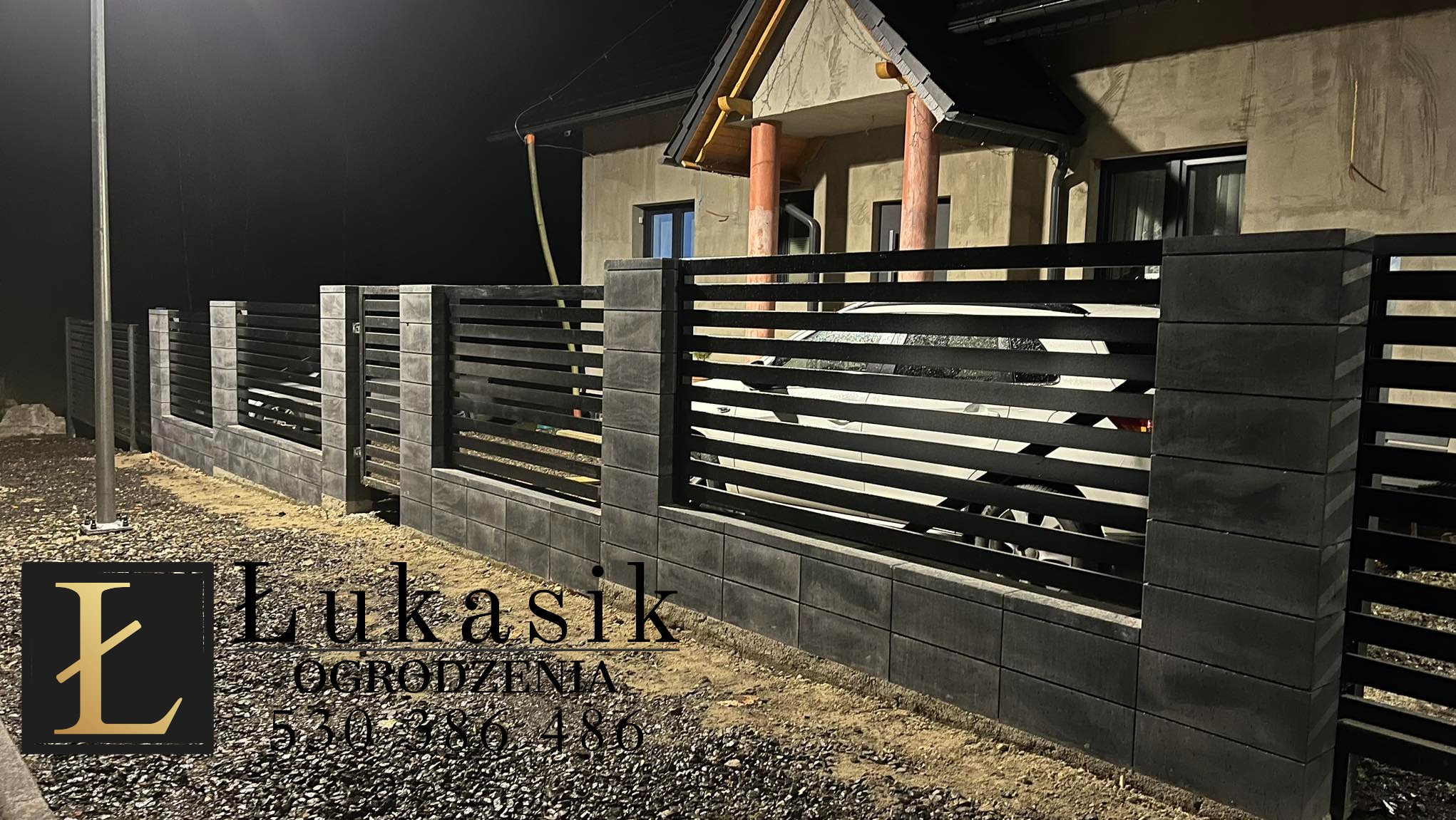 Nowoczesne ogrodzenie z poziomych, czarnych paneli i szarych, betonowych słupków, oświetlone nocą, z widocznym logotypem firmy 'Łukasik Ogrodzenia' w lewym dolnym rogu.