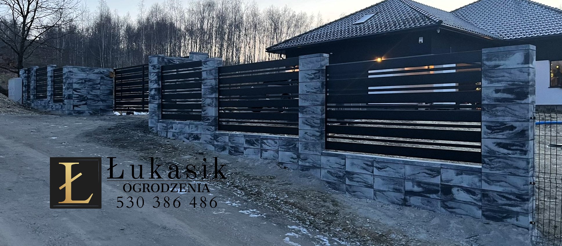 Nowoczesne ogrodzenie panelowe z betonowymi słupkami w kolorze szaro-czarnym, widoczne logo firmy Łukasik Ogrodzenia w lewym dolnym rogu, tło stanowią drzewa i budynek.
