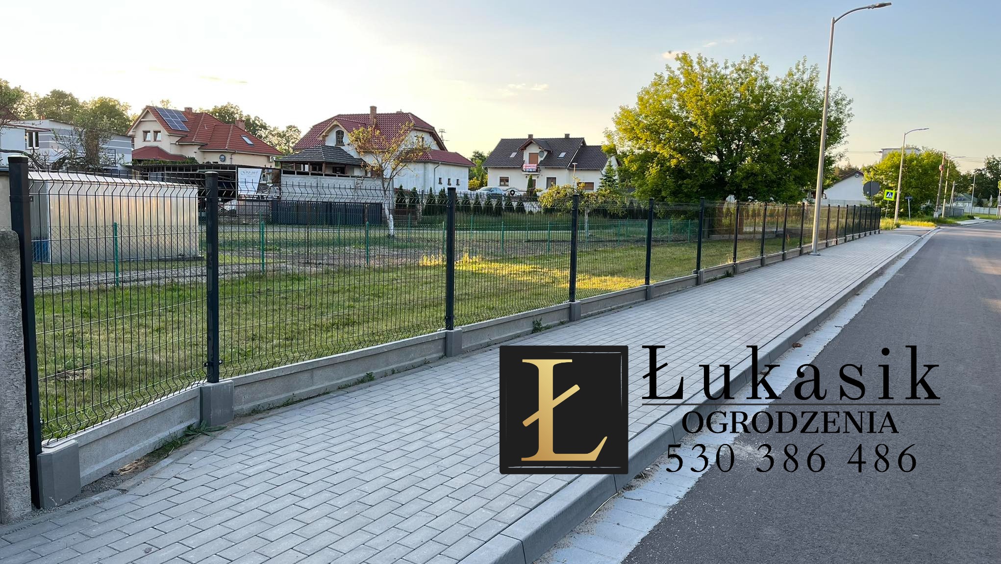 Nowoczesne ogrodzenie panelowe z podmurówką betonową, widok z chodnika, w tle domy jednorodzinne i logo firmy.