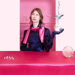 Katarzyna Fotorygo - Kobieta w satynowej bluzce i rękawiczkach pozuje przy różowym barze z martini, kulą dyskotekową i butelką z płynem u góry