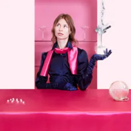 Kobieta w satynowej bluzce i rękawiczkach pozuje przy różowym barze z martini, kulą dyskotekową i butelką z płynem u góry