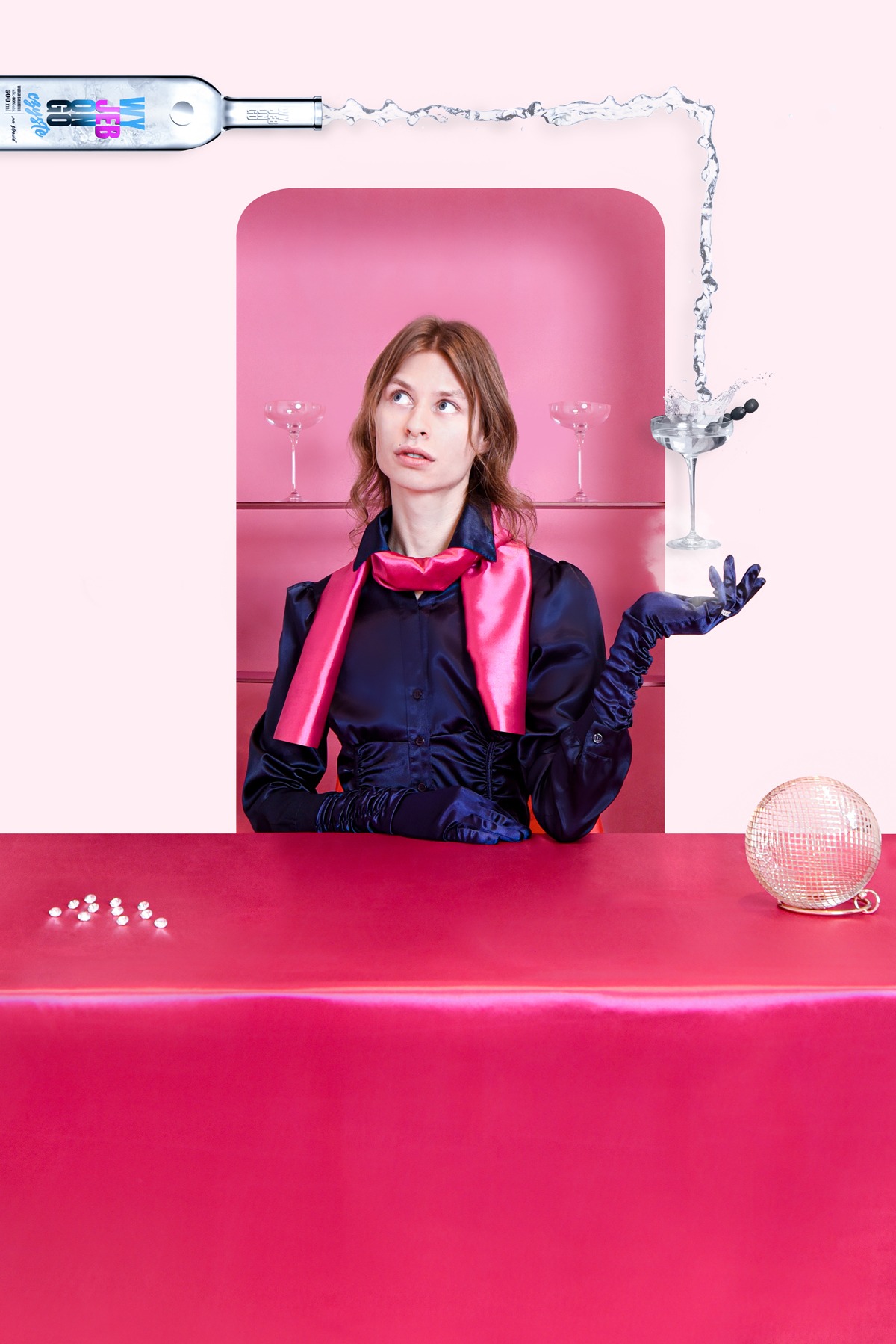 Kobieta w satynowej bluzce i rękawiczkach pozuje przy różowym barze z martini, kulą dyskotekową i butelką z płynem u góry