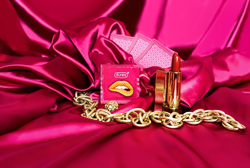 Różowa satyna drapowana z złotym łańcuchem, szminką w złotym opakowaniu, paczką prezerwatyw i kartami do gry.