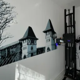 Wertykalna drukarka ścienna w trakcie nanoszenia czarno-białego obrazu zamku na białą ścianę w pomieszczeniu.