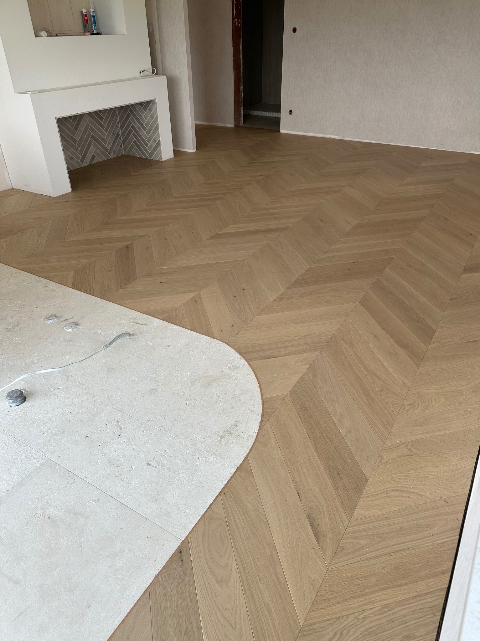 Jasny parkiet ułożony we wzór jodełki francuskiej w przestronnym wnętrzu, widoczny fragment marmurowej posadzki i obudowa kominka z szarej cegły.