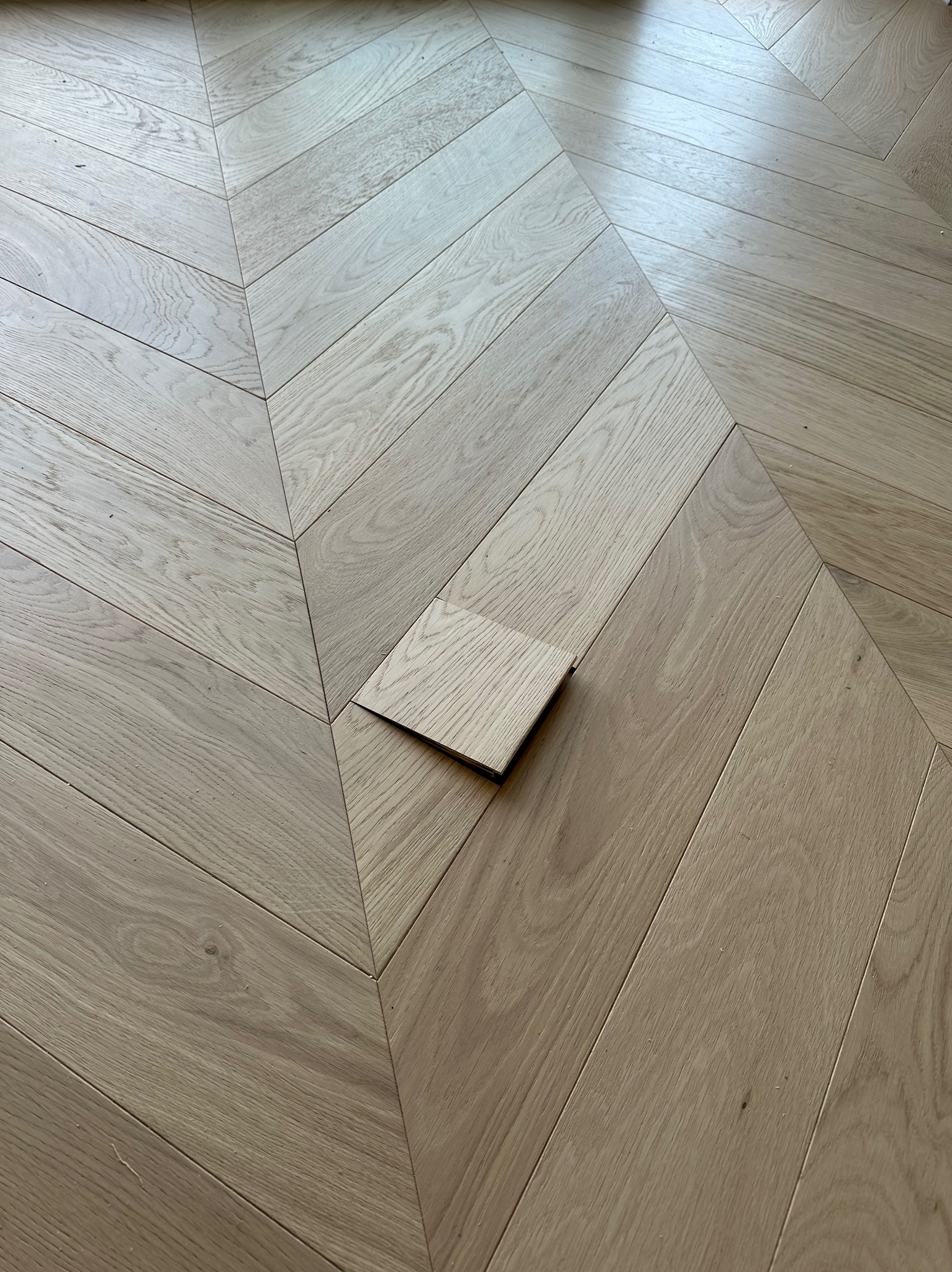 Jasny parkiet ułożony we wzór jodełki francuskiej z jednym brakującym elementem, ukazującym proces naprawy lub wymiany.