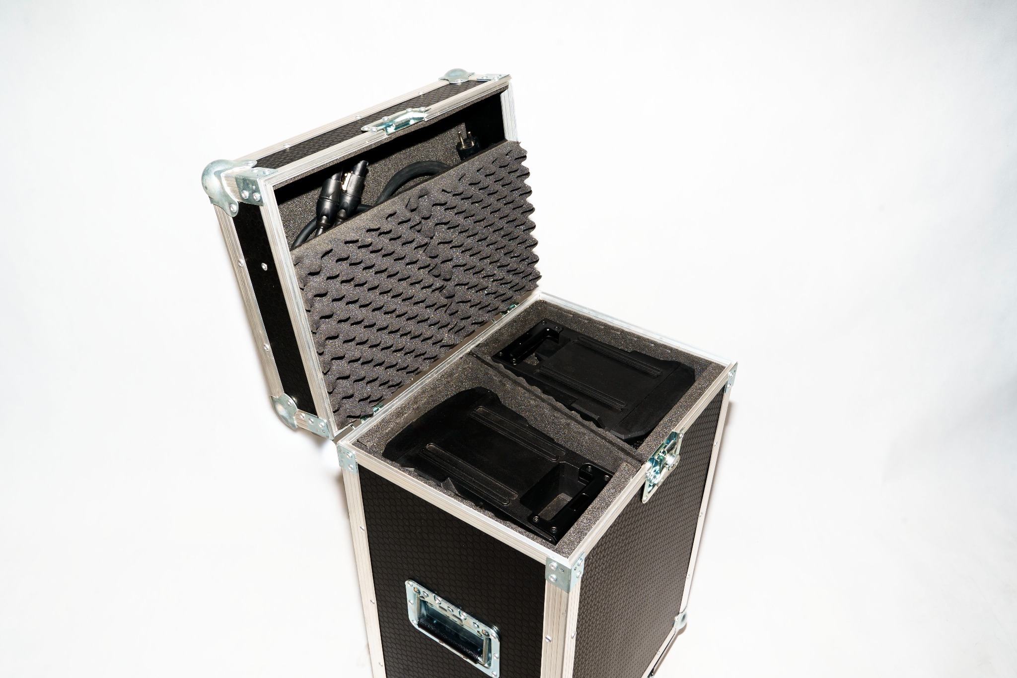 Otwarta skrzynia transportowa z piankowym wypełnieniem, widoczne kable XLR i czarne uchwyty na sprzęt.