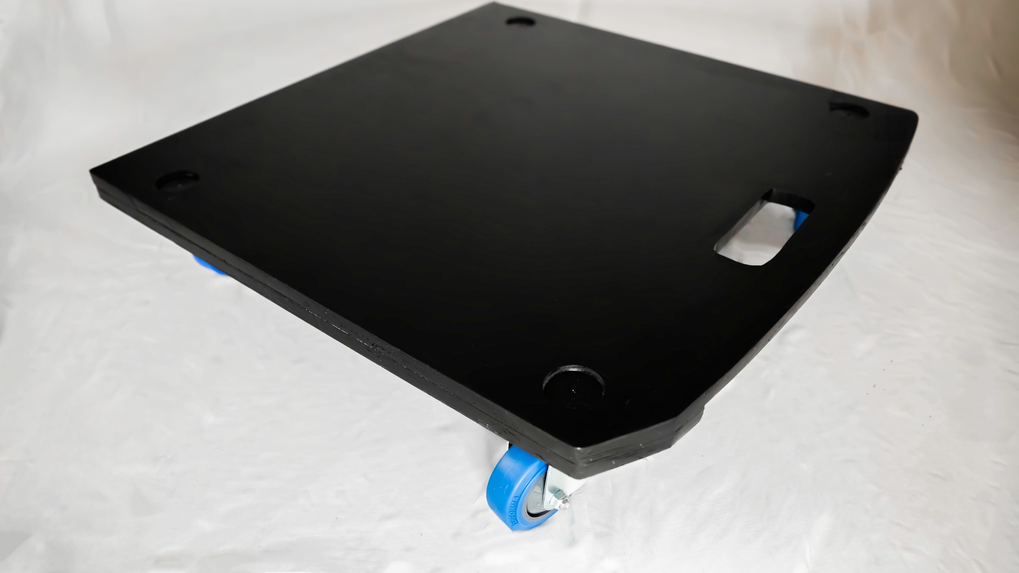 Czarna platforma transportowa na czterech niebieskich kółkach, z uchwytem na dłoń, na białym tle.