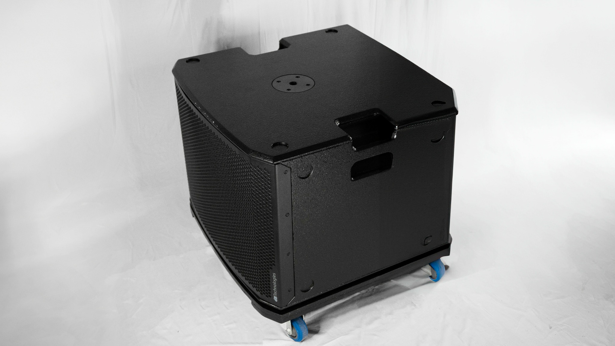 Czarny subwoofer na kółkach z metalową siatką ochronną głośnika, widoczne logo 'dB Technologies'.
