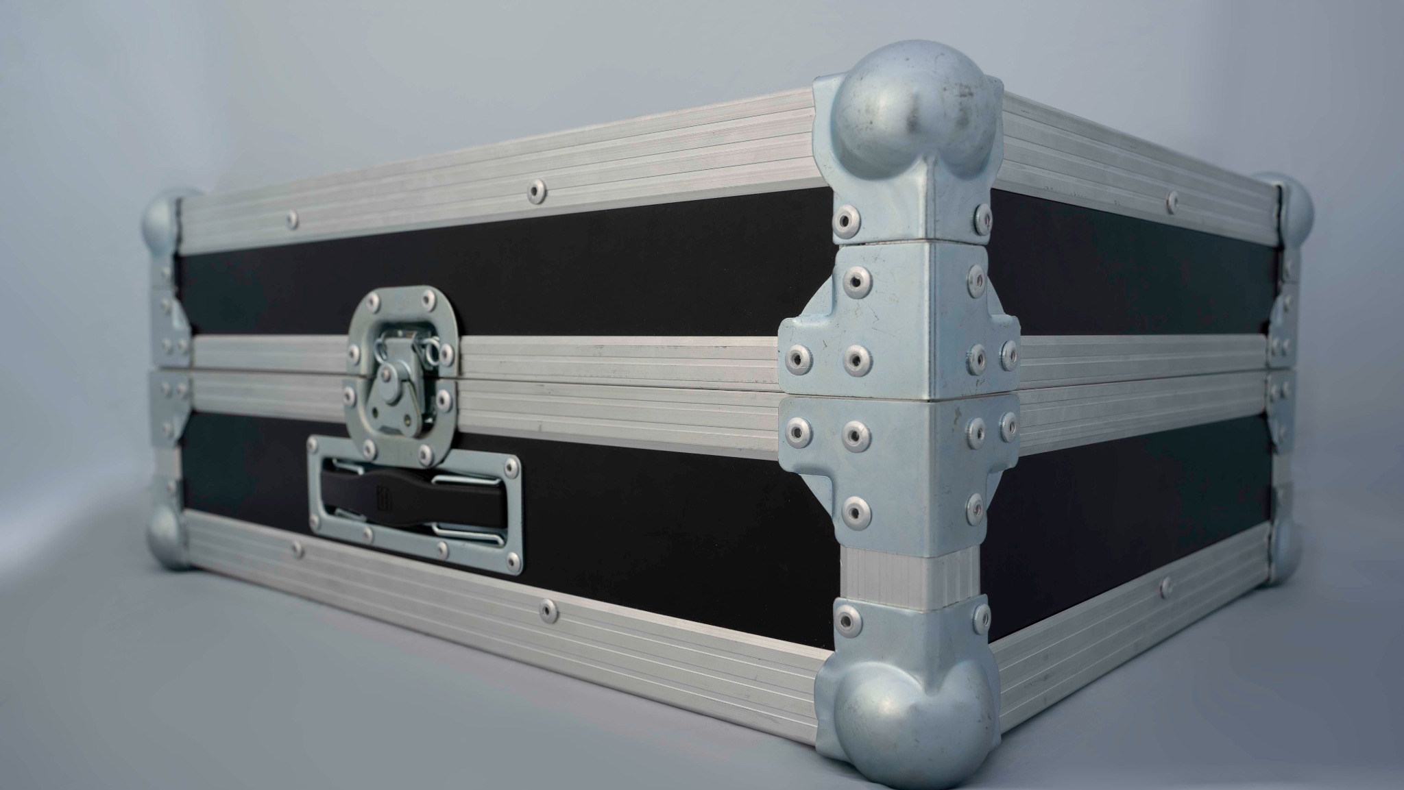 Czarna skrzynia transportowa z aluminiowymi okuciami i narożnikami, zabezpieczająca sprzęt oświetleniowy lub nagłośnieniowy.
