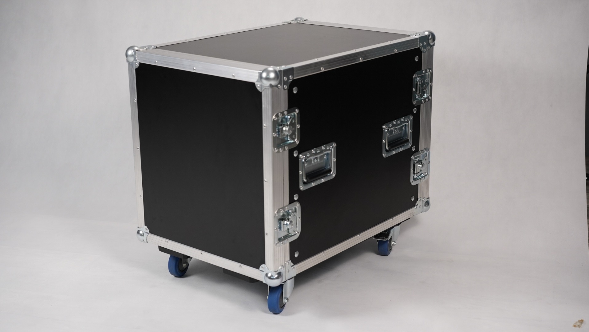 Czarna skrzynia transportowa z metalowymi okuciami i niebieskimi kółkami na białym tle.