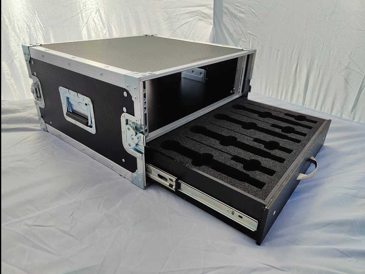 Czarna skrzynia transportowa z wysuwaną szufladą wypełnioną pianką z wyciętymi miejscami na mikrofony, widoczne metalowe okucia i szyny szuflady.