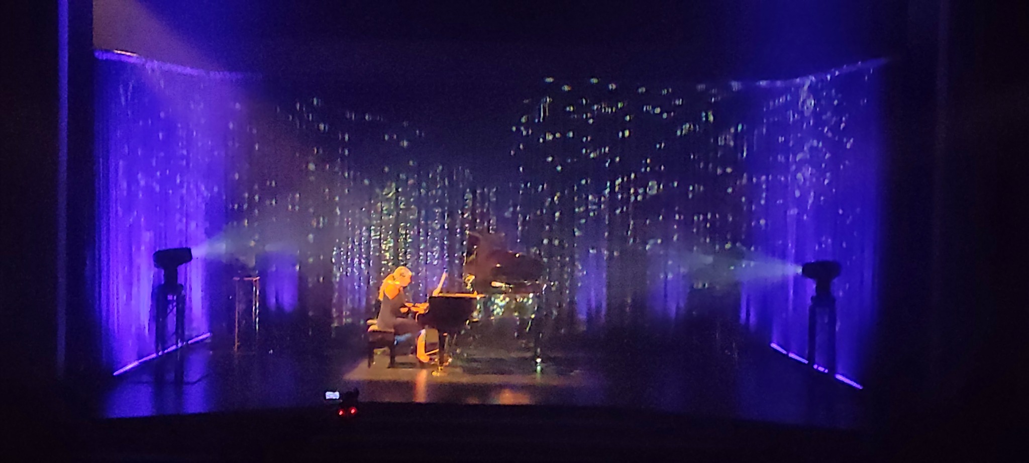 Pianistka grająca na scenie z oświetleniem punktowym w kolorze fioletowym i dekoracyjnym tłem przypominającym deszcz gwiazd.