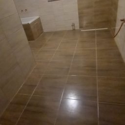 Usługi Ogólnobudowlane Michał Muzeja - Wykończona łazienka z brązowymi, prostokątnymi płytkami na ścianach i podłodze, widoczna wanna przy ścianie i okno w tle.