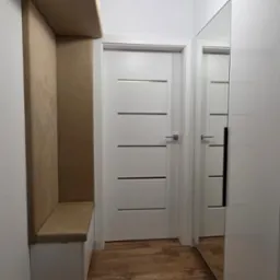 Nowoczesny przedpokój z zabudowaną szafą z lustrem, siedziskiem z tapicerowanym oparciem i drewnopodobną podłogą