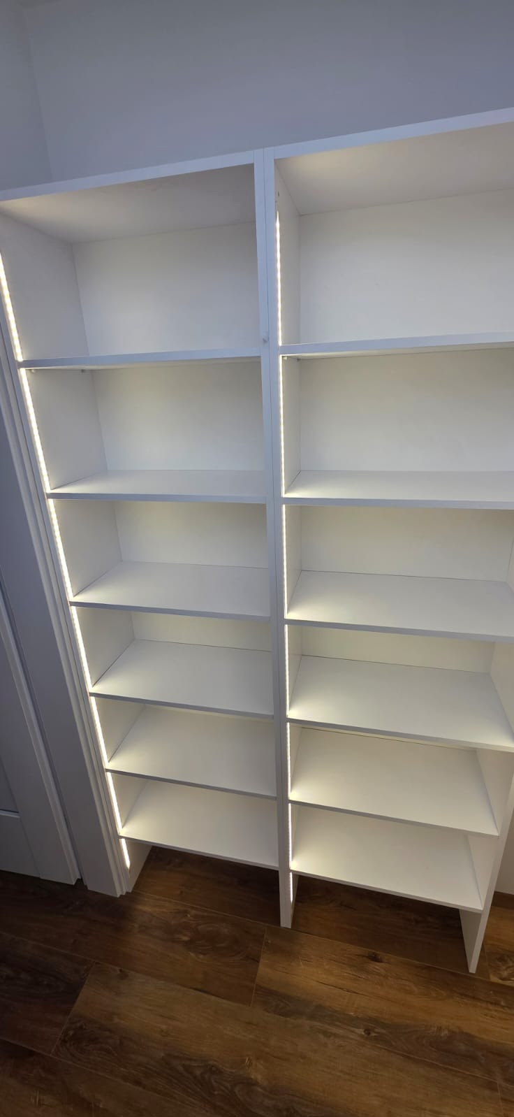 Białe, puste regały z wbudowanym oświetleniem LED, zamontowane we wnęce, widoczne z perspektywy podłogi z paneli.