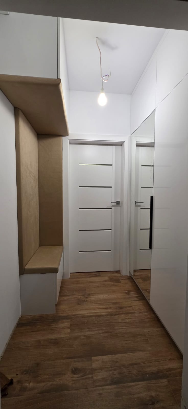 Nowoczesny przedpokój z zabudowaną szafą z lustrem, siedziskiem z tapicerowanym oparciem i drewnopodobną podłogą