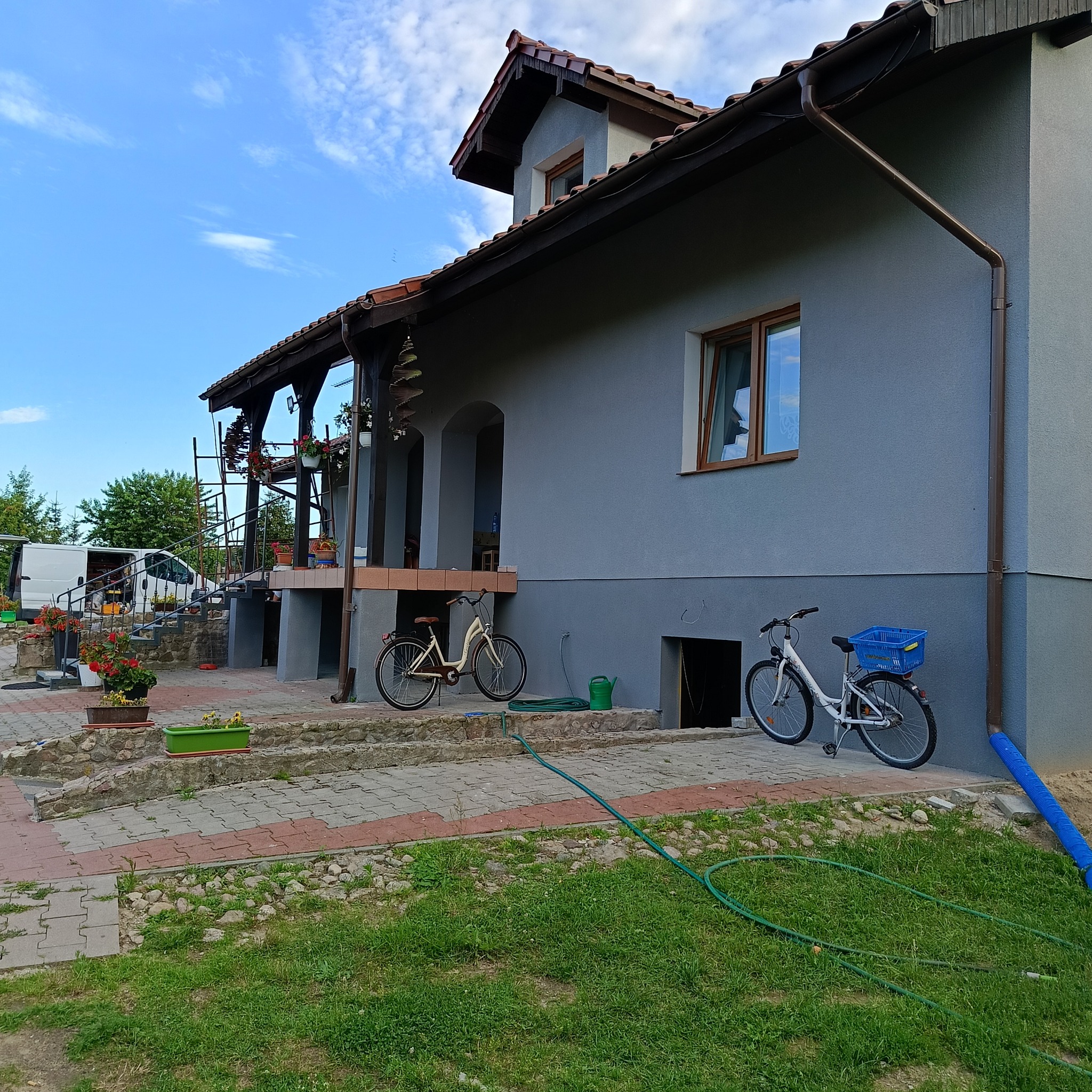 Szary dom jednorodzinny w Jastrowiu po malowaniu elewacji, z widocznymi rynnami, rowerami i zielonym wężem ogrodowym na trawniku.