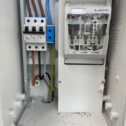 VOLT-TOM - Wnętrze skrzynki elektrycznej z zainstalowanymi bezpiecznikami i wyłącznikiem, widoczne przewody w różnych kolorach, elementy montażowe i oznaczenia producenta Apator.