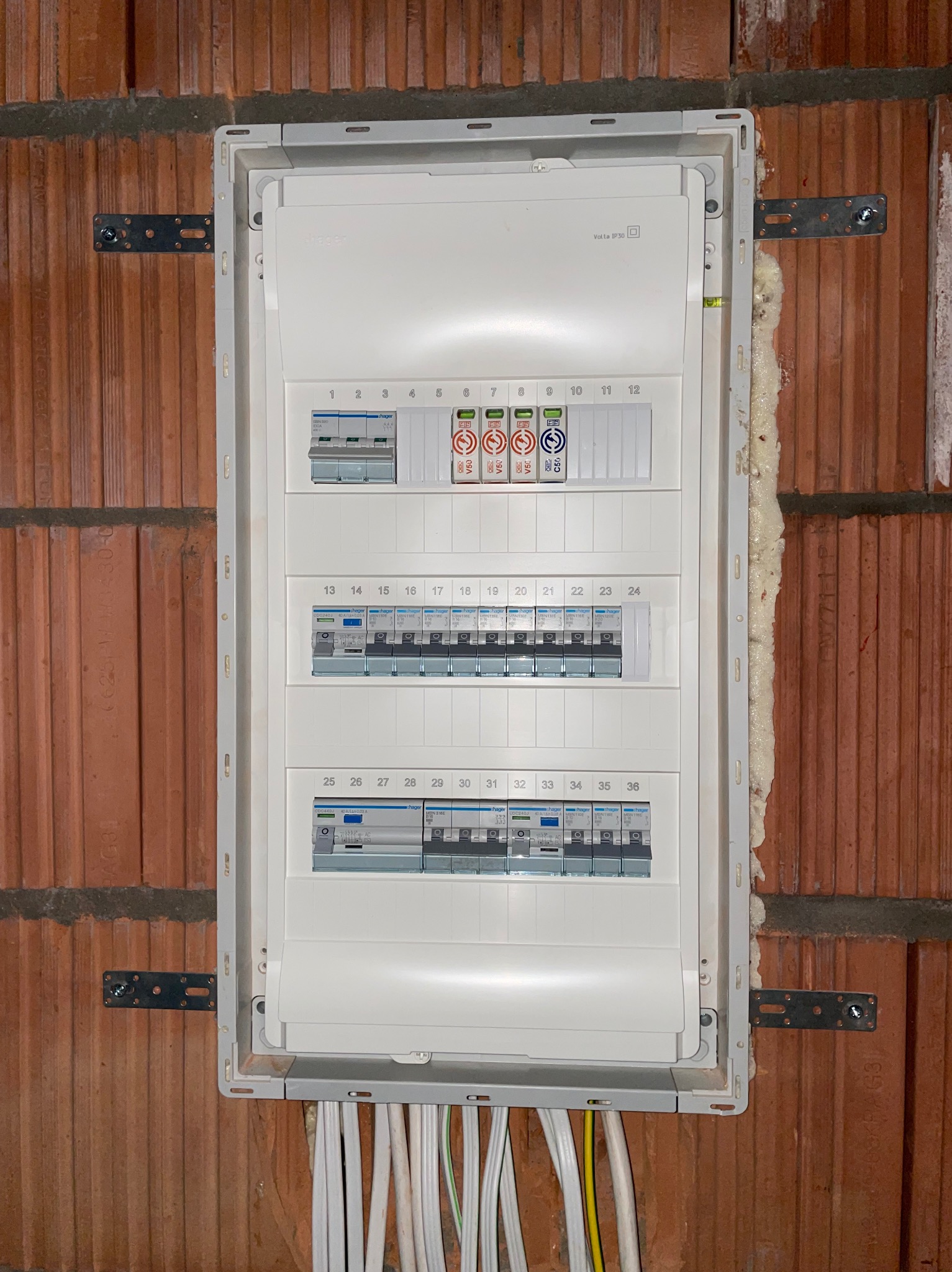 Rozdzielnica elektryczna Hager Volta IP30 zamontowana na ceglanej ścianie z widocznymi przewodami i pianką montażową uszczelniającą obudowę.