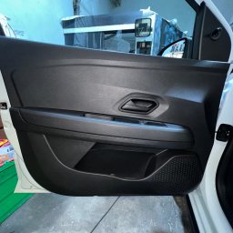 CAR MAX - Wnętrze samochodu: czarny panel drzwi z fakturą włókna węglowego, widok z bliska, na tle warsztatu.