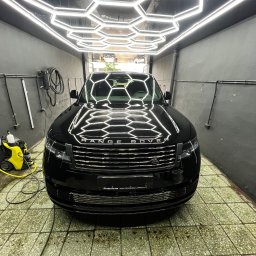 NOVA Detailing. Myjnia ręczna, korekta lakieru, pranie tapicerki - Lśniący czarny Range Rover w pomieszczeniu do pielęgnacji aut, z heksagonalnymi lampami LED odbijającymi się na idealnie czystej karoserii. Obok widoczny sprzęt Karcher.