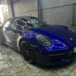 NOVA Detailing. Myjnia ręczna, korekta lakieru, pranie tapicerki - Ciemnoniebieskie Porsche 911 cabriolet po myciu, stojące na mokrej, kafelkowej posadzce w myjni, z widocznymi odbiciami świateł na karoserii.