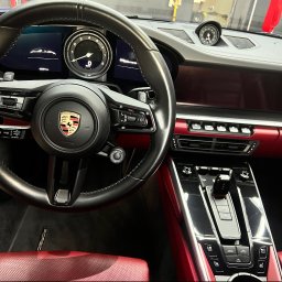 NOVA Detailing. Myjnia ręczna, korekta lakieru, pranie tapicerki - Wnętrze luksusowego Porsche z czerwoną perforowaną tapicerką i deską rozdzielczą, lśniące czystością po profesjonalnym detailingu we Wrocławiu.