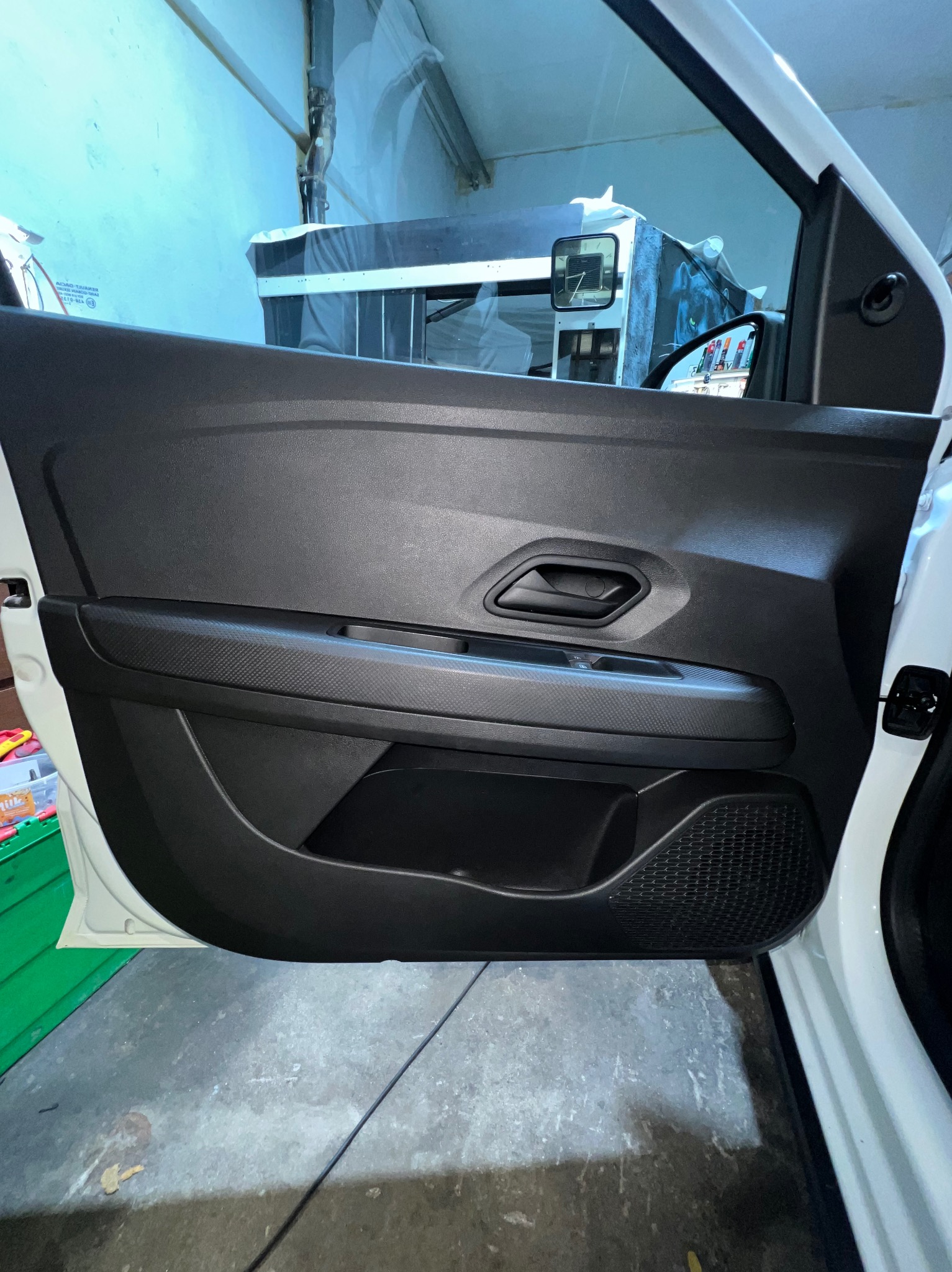 Wnętrze samochodu: czarny panel drzwi z fakturą włókna węglowego, widok z bliska, na tle warsztatu.