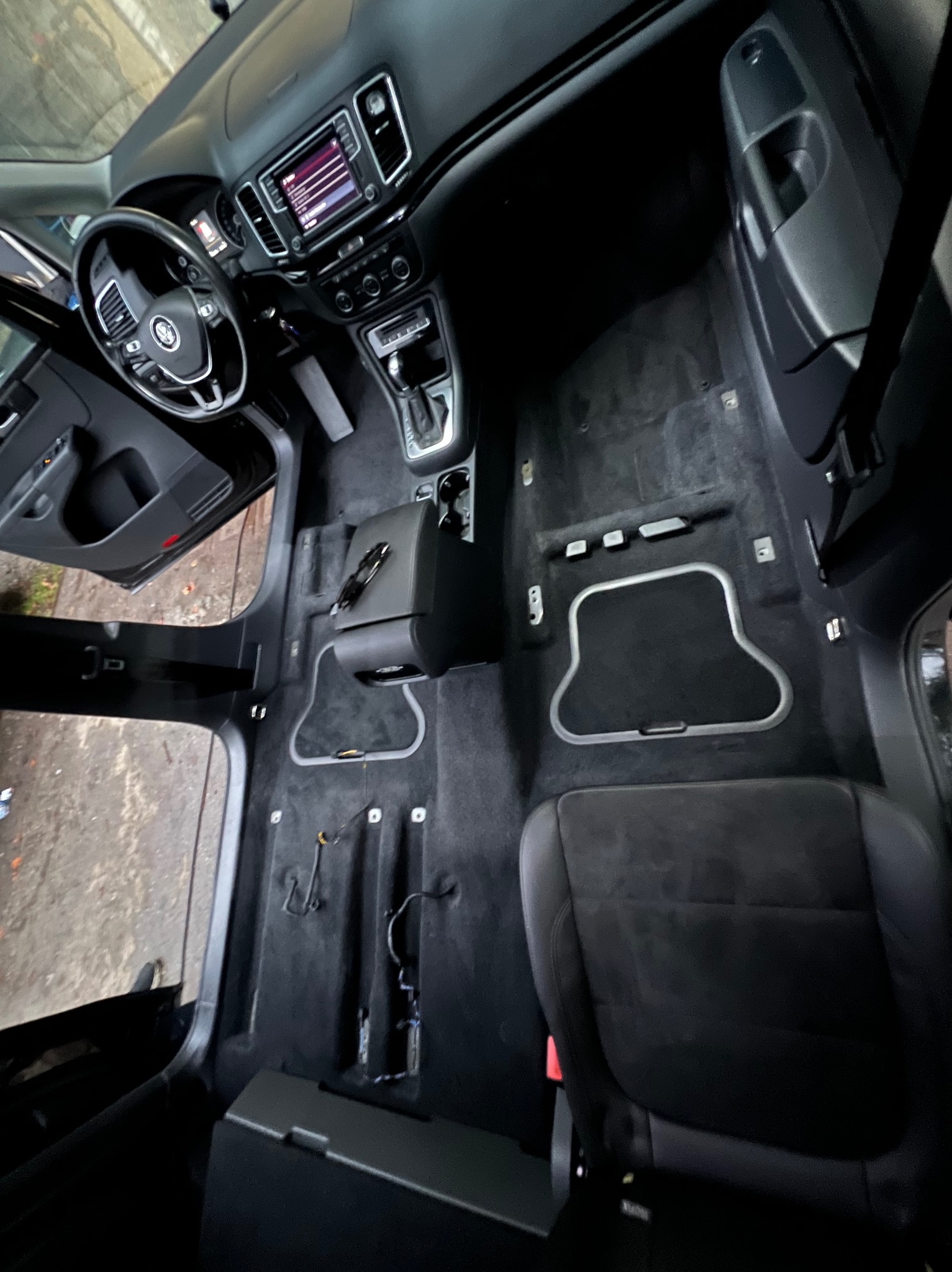 Wnętrze samochodu z wyjętymi fotelami, przygotowane do czyszczenia wykładziny podłogowej, widoczne elementy deski rozdzielczej i kierownica.