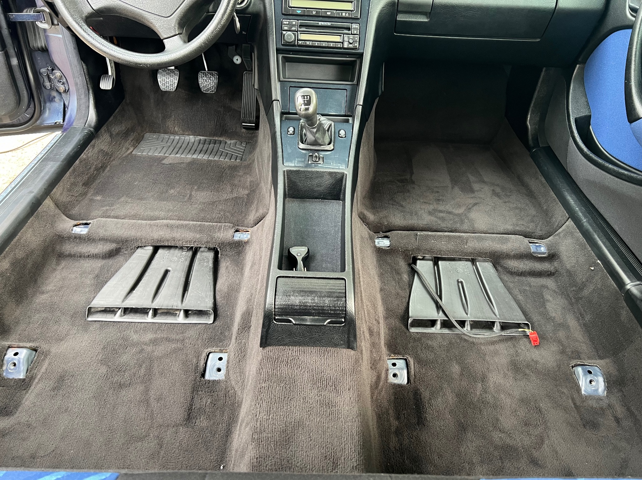 Wnętrze samochodu z wyjętymi elementami i odsłoniętą tapicerką podłogową, przygotowane do czyszczenia lub renowacji.