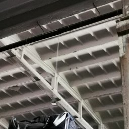 GRACO GRACJAN KOZIEŁ - Wnętrze hali magazynowej z betonowym stropem kasetonowym, widoczne worki typu big bag z materiałem sypkim. Ujęcie z dołu, oświetlenie sztuczne.