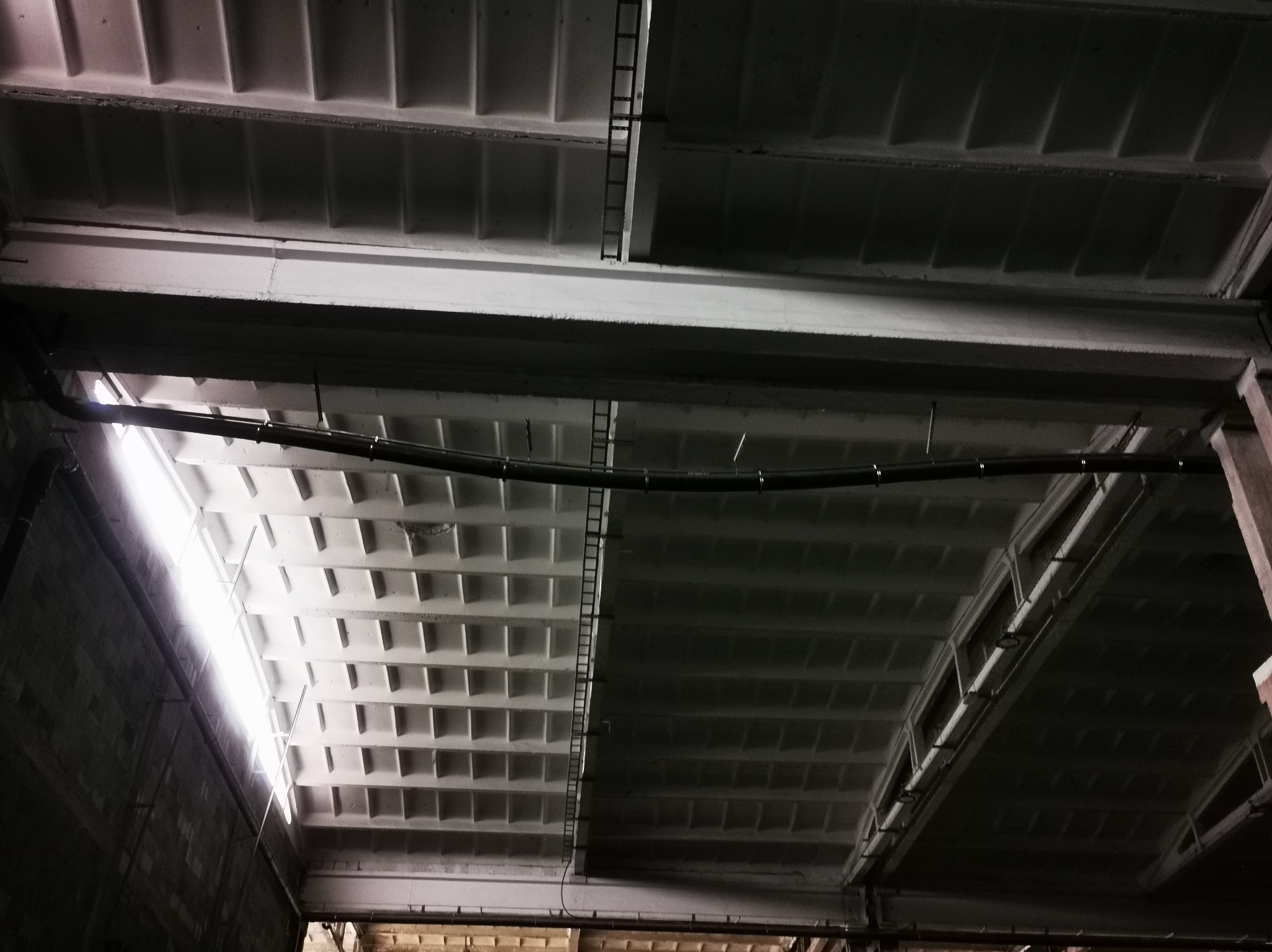 Betonowy strop z instalacjami w hali w Będzinie. Widoczne żebra stropowe, rury instalacyjne i oświetlenie. Ujęcie z dołu, podkreślające surowość i funkcjonalność konstrukcji.