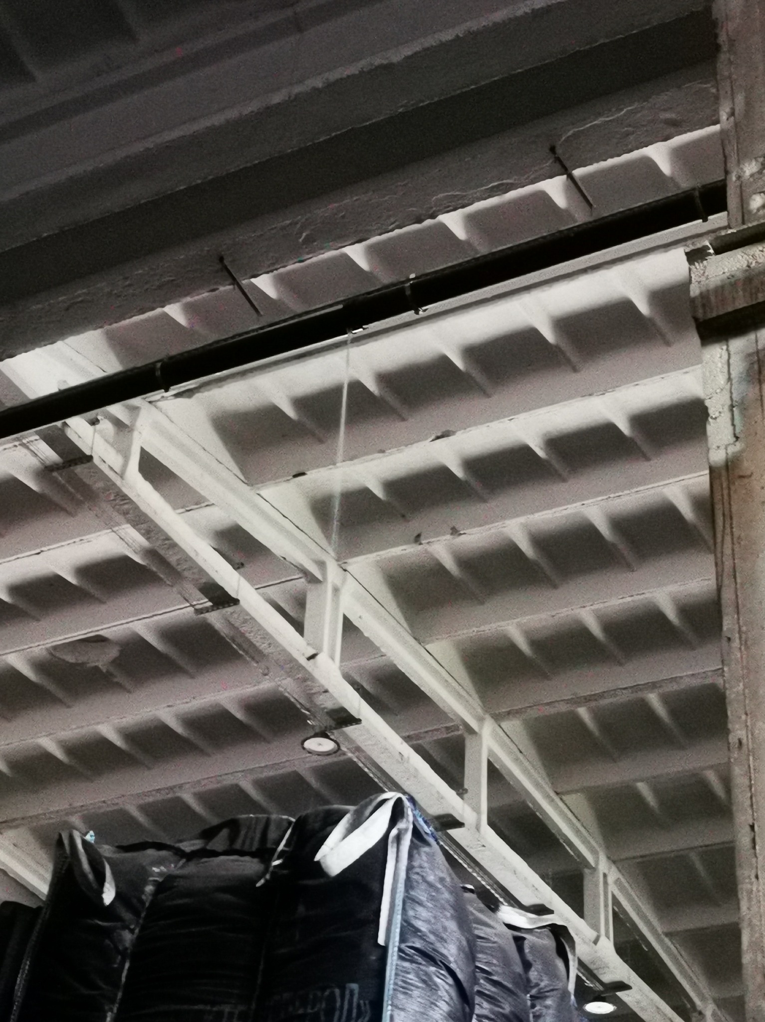 Wnętrze hali magazynowej z betonowym stropem kasetonowym, widoczne worki typu big bag z materiałem sypkim. Ujęcie z dołu, oświetlenie sztuczne.