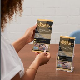 Patrycja Ciborowska - Kobieta trzyma ulotkę z logo i informacjami o Daniel Danielsky, obok stojak z ulotkami na drewnianym stole.