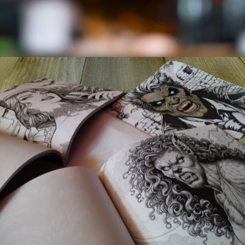 Otwarte książki z ilustracjami fantasy, w tym wizerunki wilkołaka i zombie, leżące na drewnianej powierzchni.