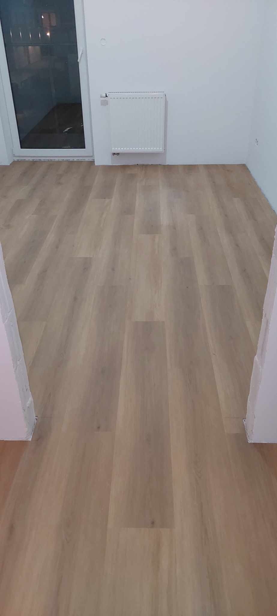 Jasne panele podłogowe ułożone w nowym pokoju z białymi ścianami i grzejnikiem, widok z poziomu podłogi.