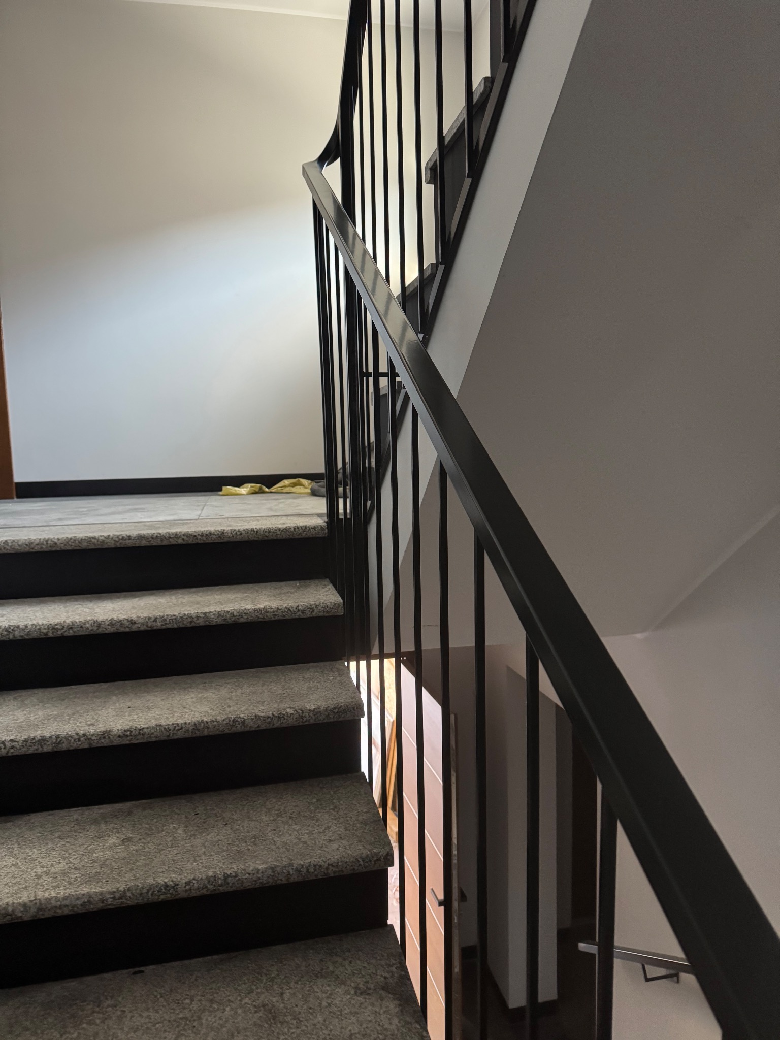 Klatka schodowa z szarymi stopniami i czarną, minimalistyczną balustradą z pionowych prętów, widok z dołu do góry.