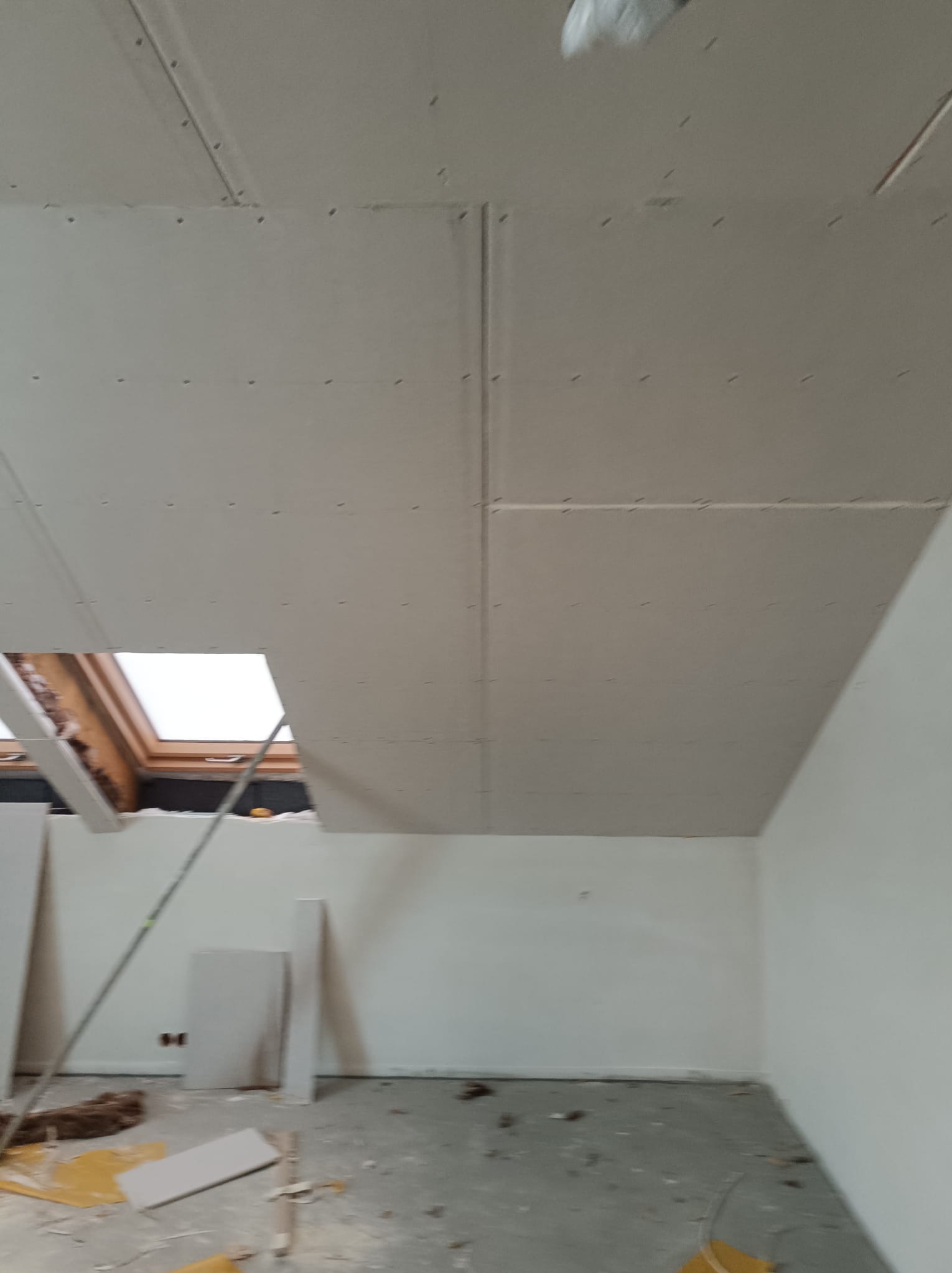 Montaż płyt karton gips na poddaszu, widoczne okno dachowe, surowe wykończenie, ślady po pracach na podłodze.